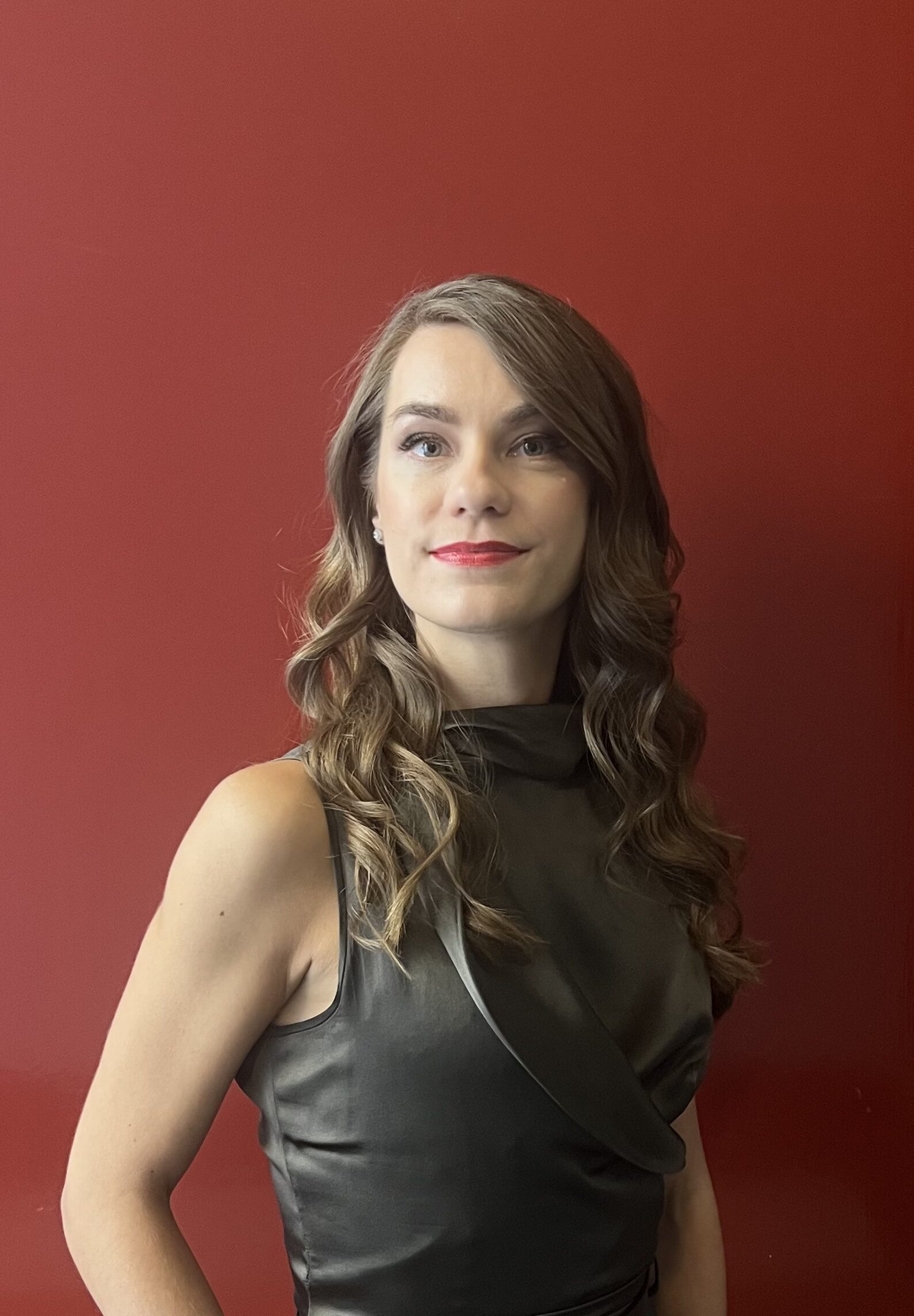 Portrait of Triin, fashion designer and founder, standing against a red background, wearing a sleeveless black top.